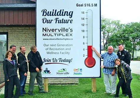 Heather Miller, Eric King, Clayton Smeltz, John Funk, Clarence Braun, Myron Dyck, and Libby Hanna raise the multiplex fundraising thermometer outside of the town office